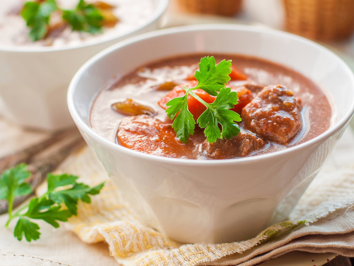 Auf einem Geschirrtuch befindet sich eine Schüssel mit einer Gulasch Suppe. Henkelmann Gastronomiebetrieb